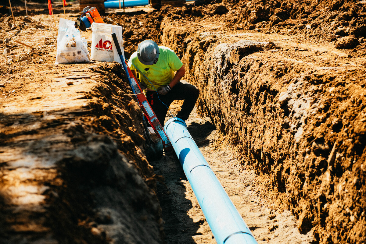 Worker crouching over pipe in a trench